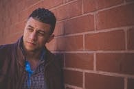Confident male model in leather jacket posing against a brick wall.